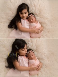 baby girl laying down big sister getting kissed