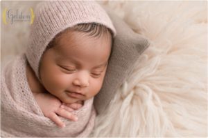 baby girl wrapped wearing pink bonnet on a newborn pillow