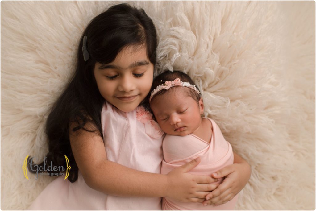 newborn baby girl laying down on white rug with big sister
