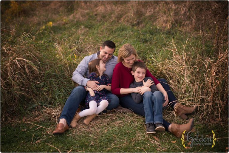 family of four seated in the grass ticking each other