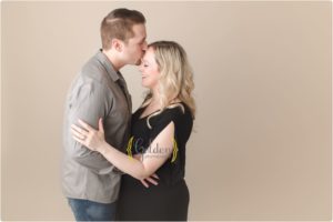 pregnant couple kissing and smiling in Lake County IL photography studio
