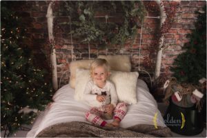 child sits on Christmas bed for mini sessions in Chicago suburbs