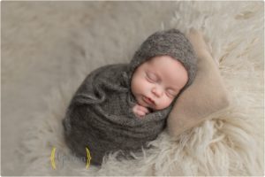 baby boy swaddled in grey on fuzzy rug during newborn photo session with best photographer in Lake County IL