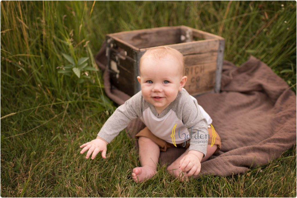 smiling little boy sitting in tall grass in Lake County IL forest preserve
