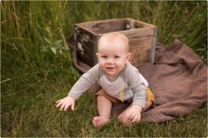 smiling little boy sitting in tall grass in Lake County IL forest preserve