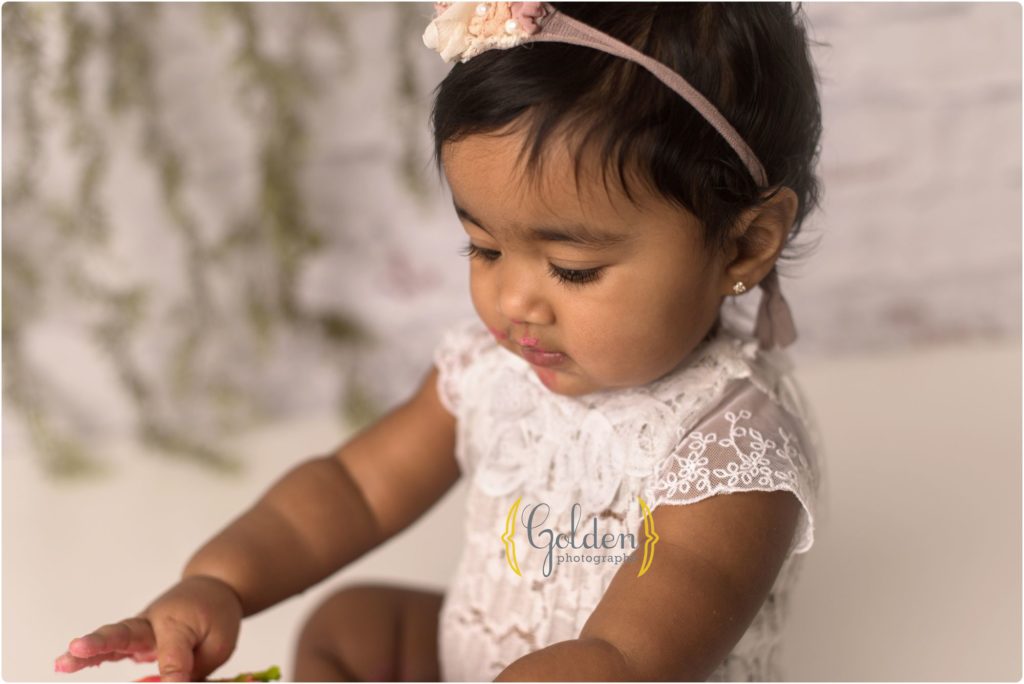 little girl looking down at cake for first birthday photo session in Lake County Illinois