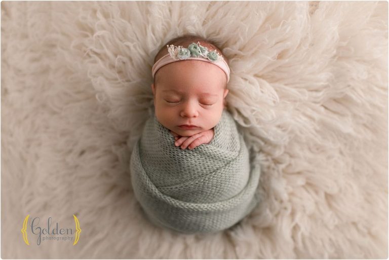 newborn girl wearing green on fuzzy rug in Lake County IL best newborn photographer studio