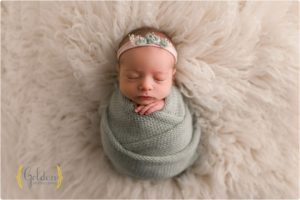 newborn girl wearing green on fuzzy rug