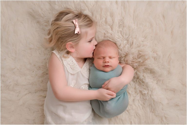sibling gently holding newborn baby on floor