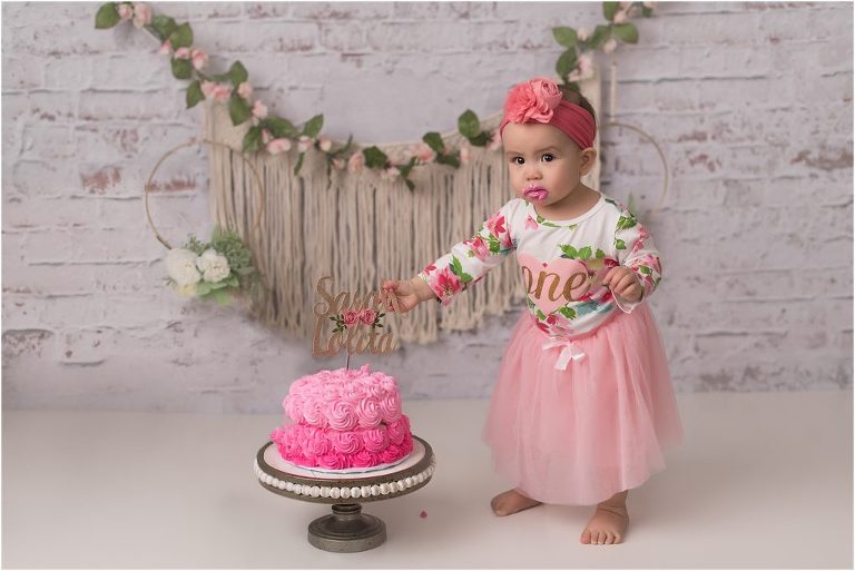 1 year old standing by 1st birthday cake in photography studio near Chicago