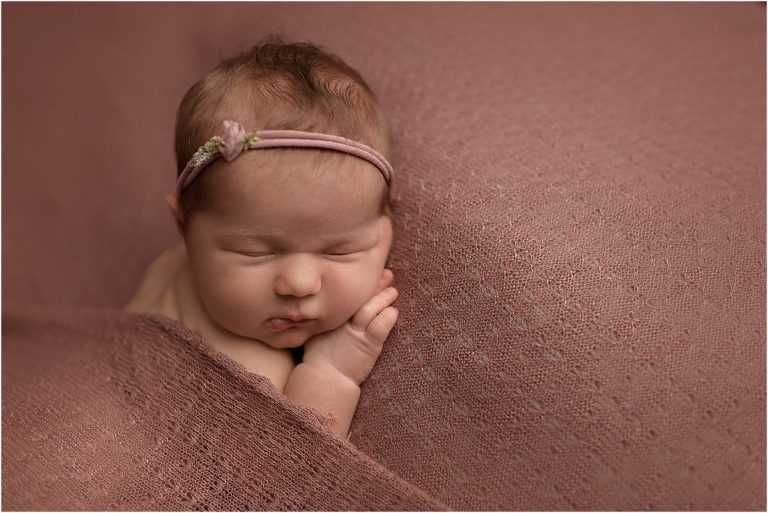 baby girl sleeping on rose color fabric for newborn photo session