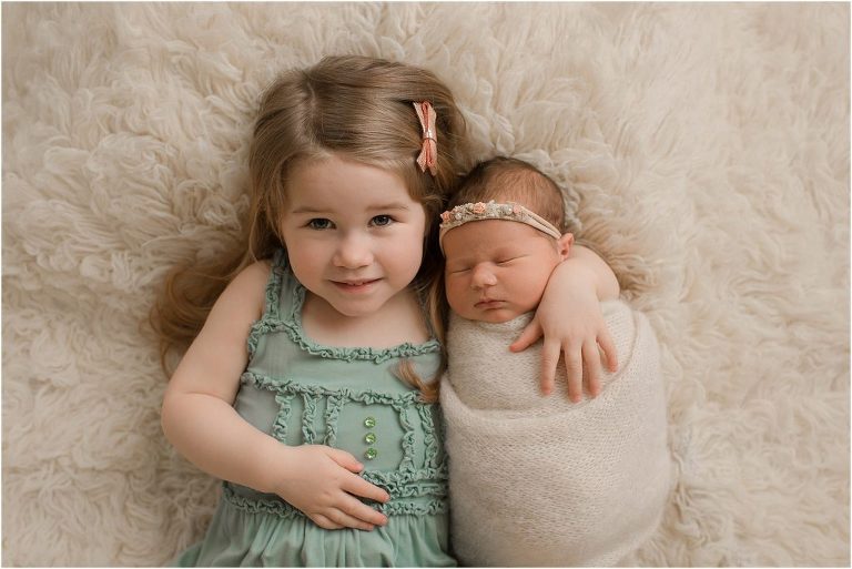 big sister holding swaddled baby sister during newborn photoshoot