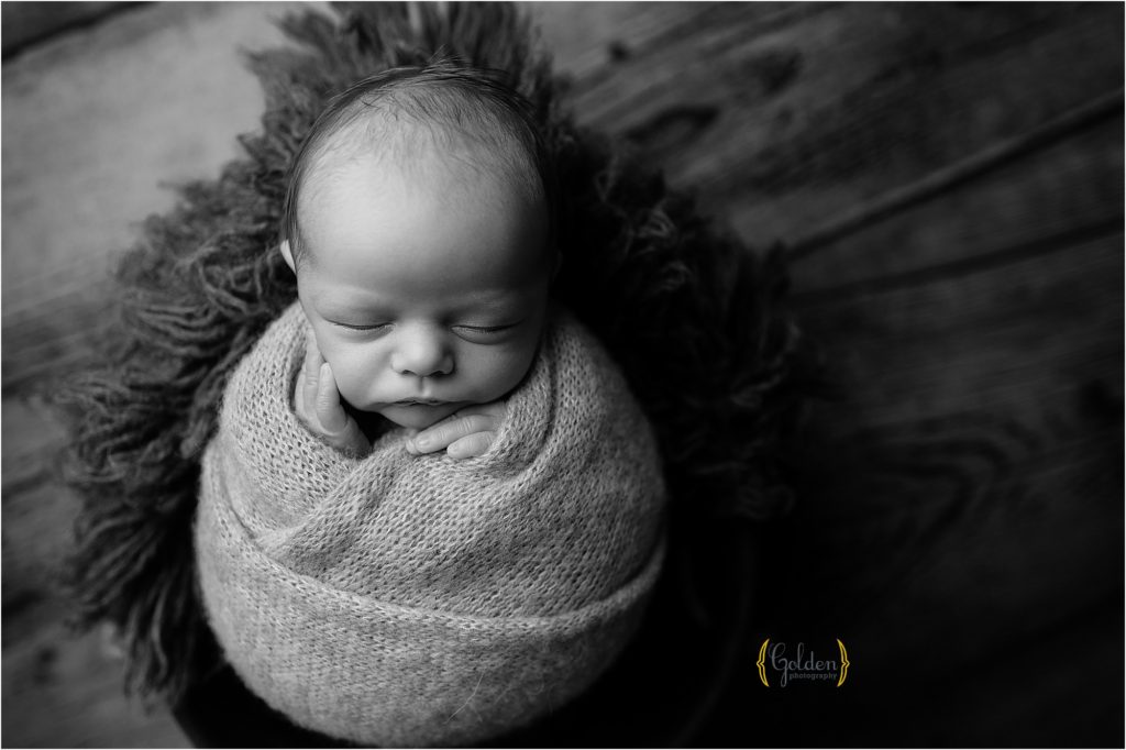 black and white of baby cupping face while wrapped up