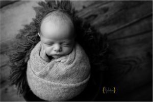 black and white of baby cupping face while wrapped up