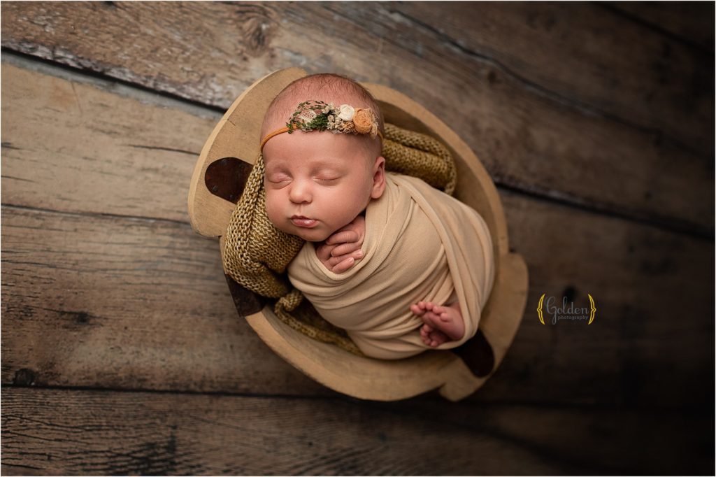baby girl swaddled in yellow posed in a bowl at Golden Photography studio in Illinois