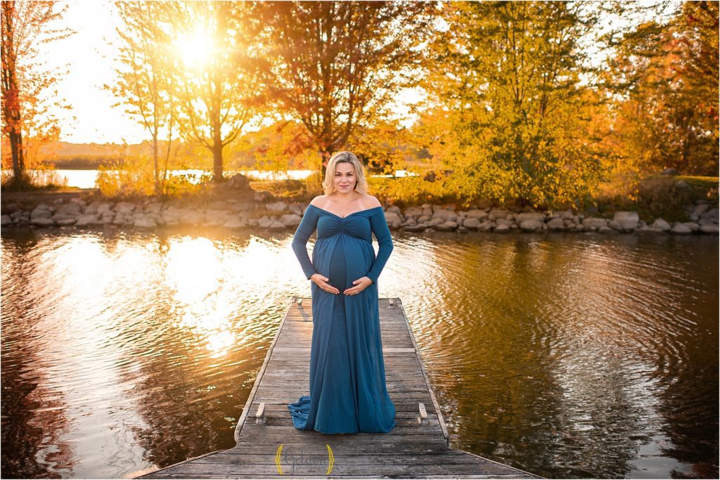 mom wearing a blue dress standing on a dock at sunset