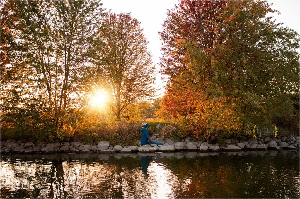 mom standing along on rocks by the water at sunset for maternity photographer