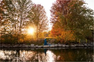 mom standing along on rocks by the water at sunset for maternity photographer