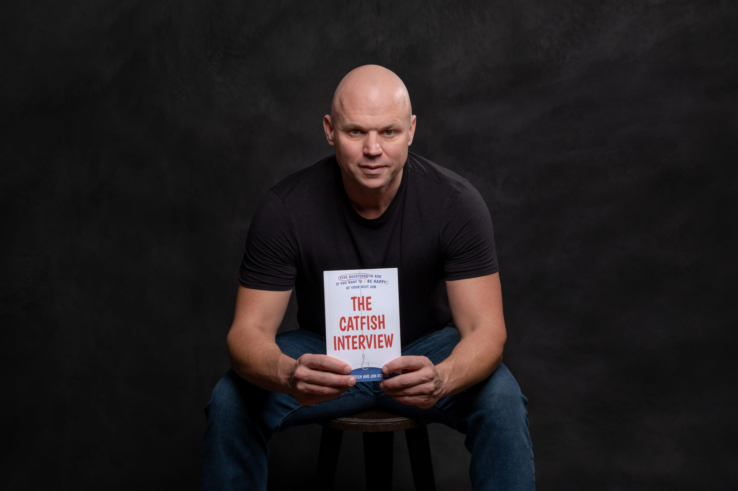 author sits on stool holding book on dark backdrop in Lake Zurich studio